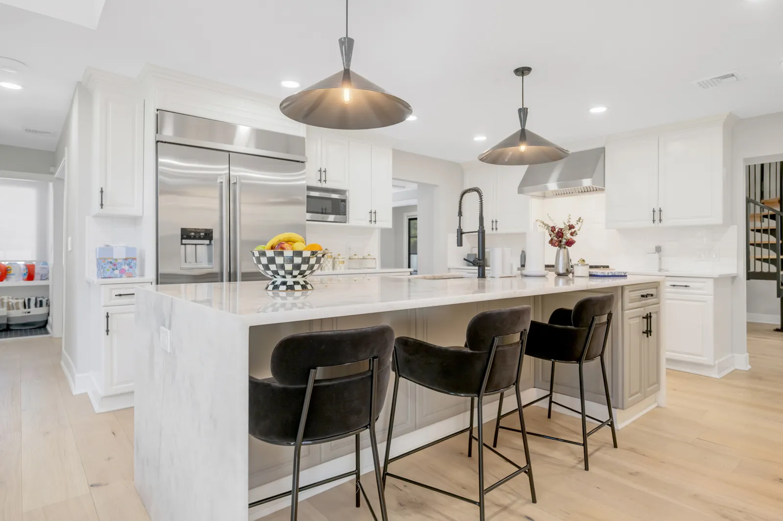 Kitchen after renovation — custom white cabinetry, marble waterfall island, and wide-plank oak flooring