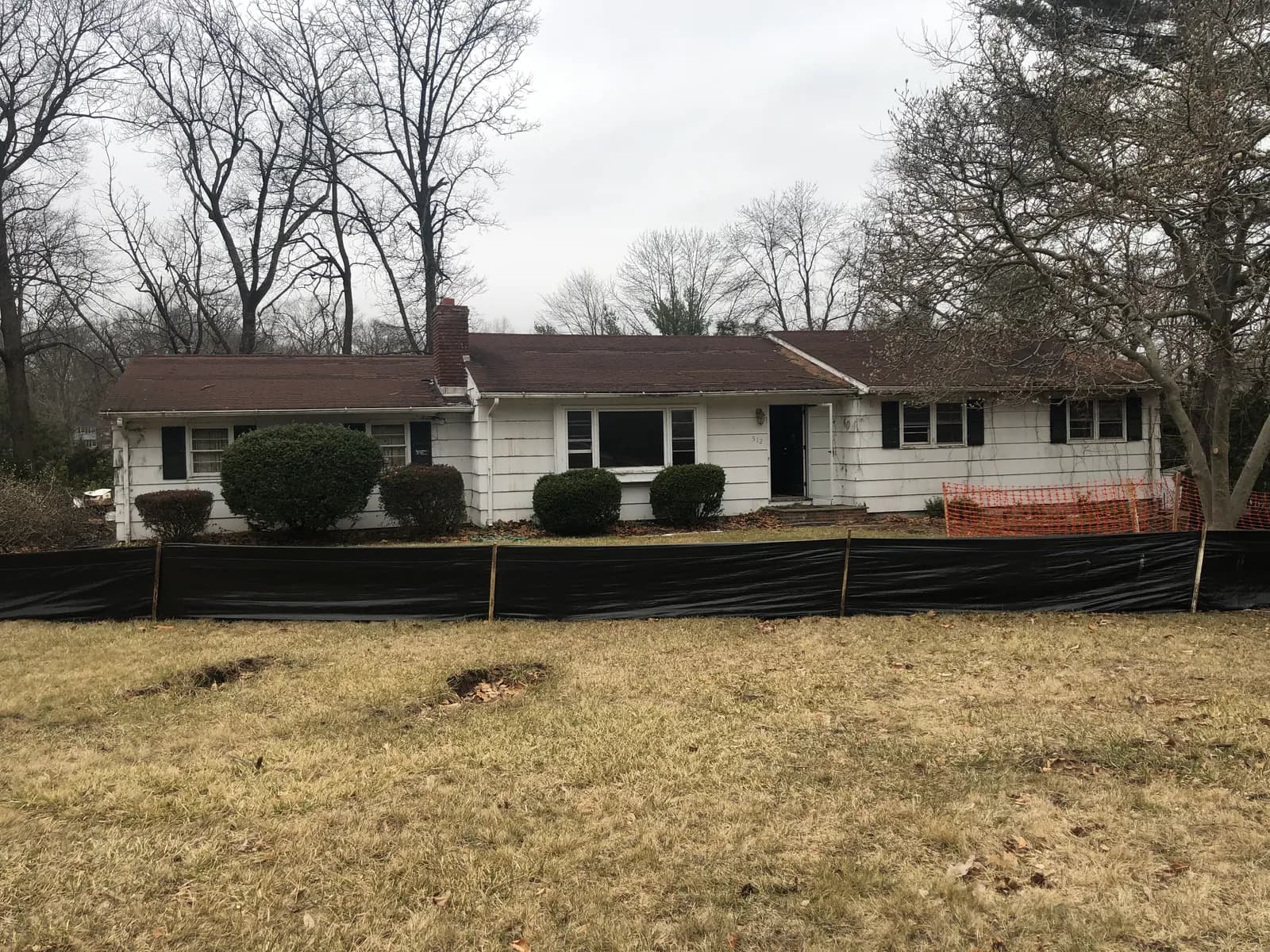 Original ranch home behind silt fencing before teardown