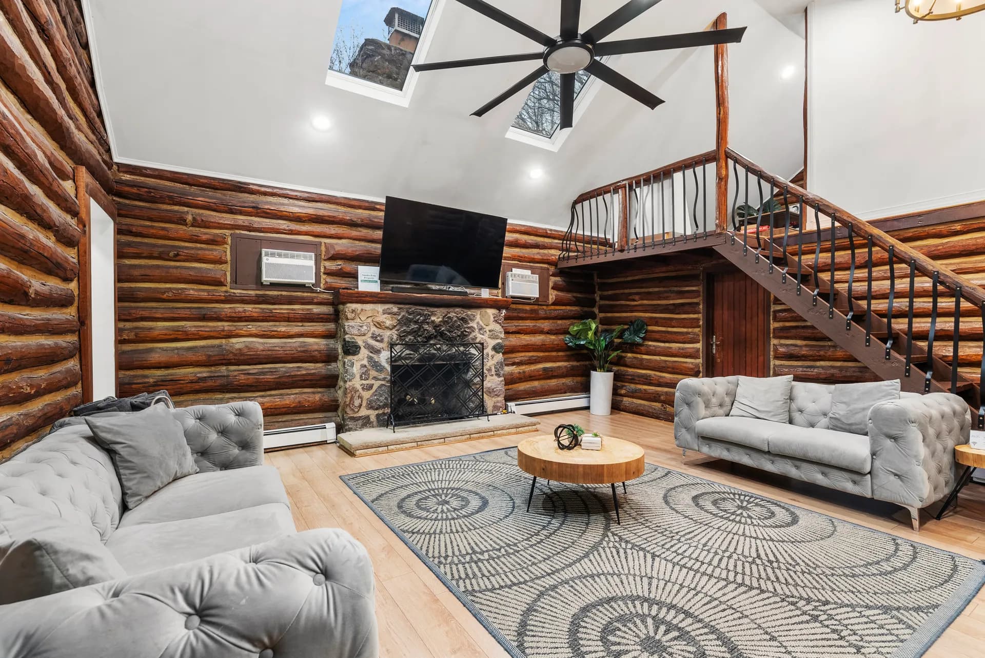 Finished living room — stone fireplace, loft above, restored log walls