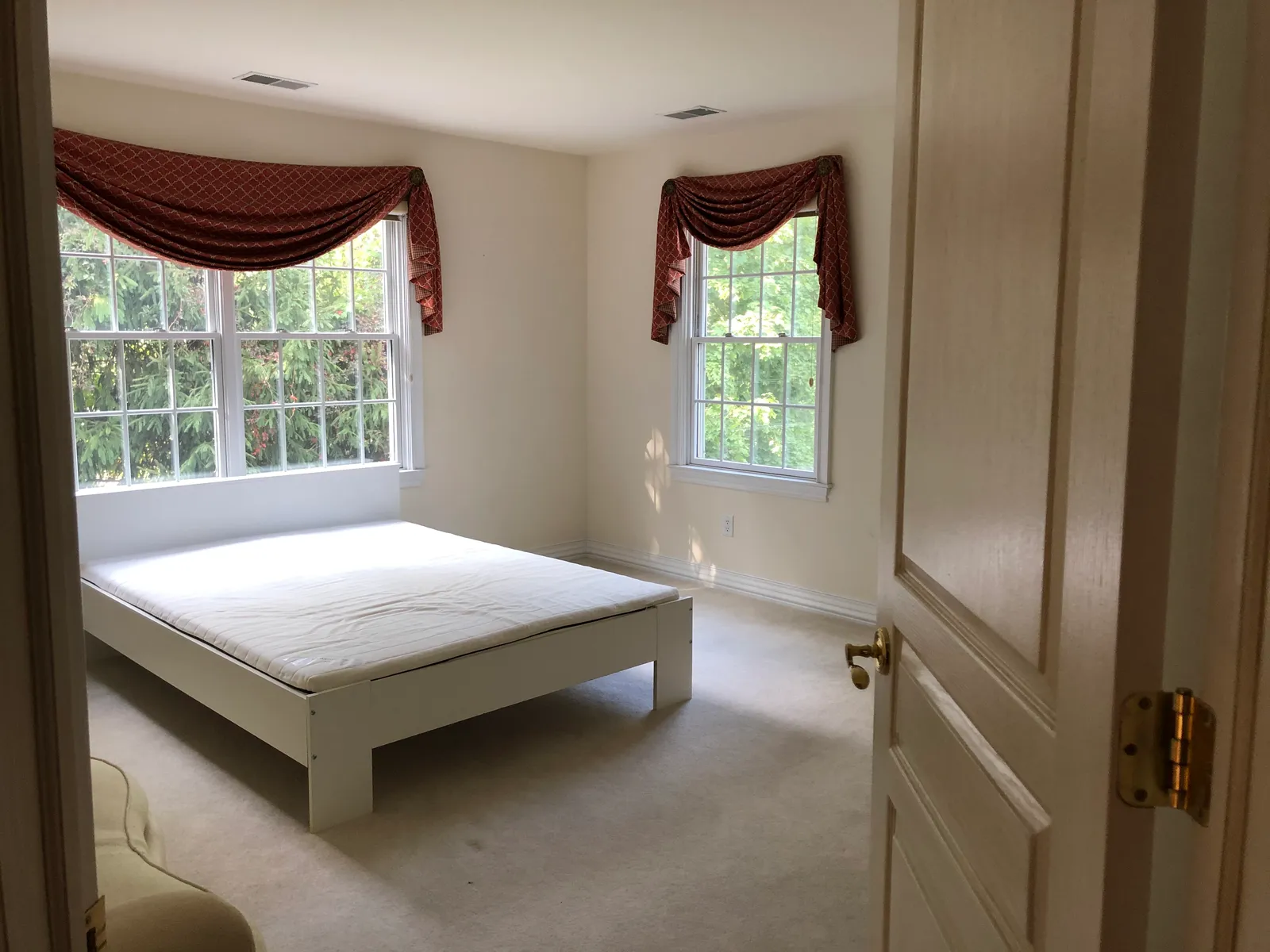 Bedroom before renovation — dated window treatments and flat walls